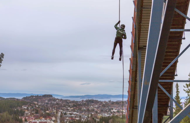 Person in helmet hanging from bridge overlooking homes and sea